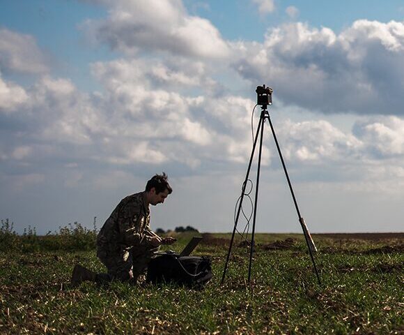 soldier in green fatigues sets up weather station in field on a tripod
