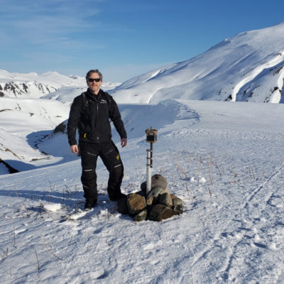 Man stands beside micro weather station on snow- and ice-covered slopes of volcano in Alaska