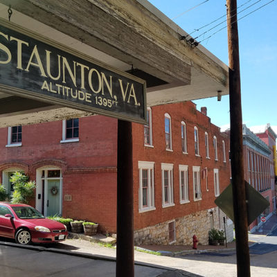 sign showing the town name of stauton, virginia and the population with a small downtown street in the background
