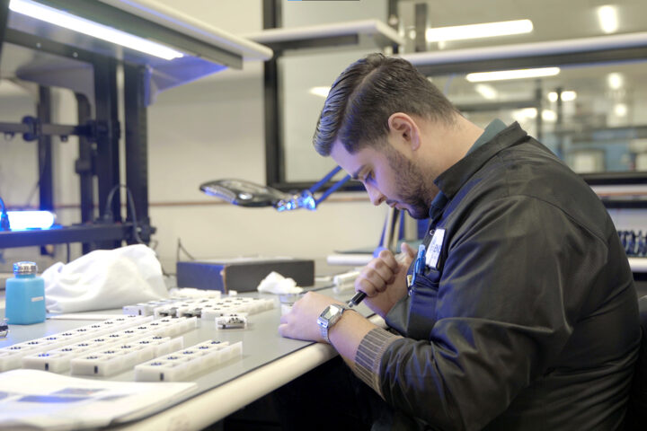 man assembles electronics in production environment with florescent light overhead