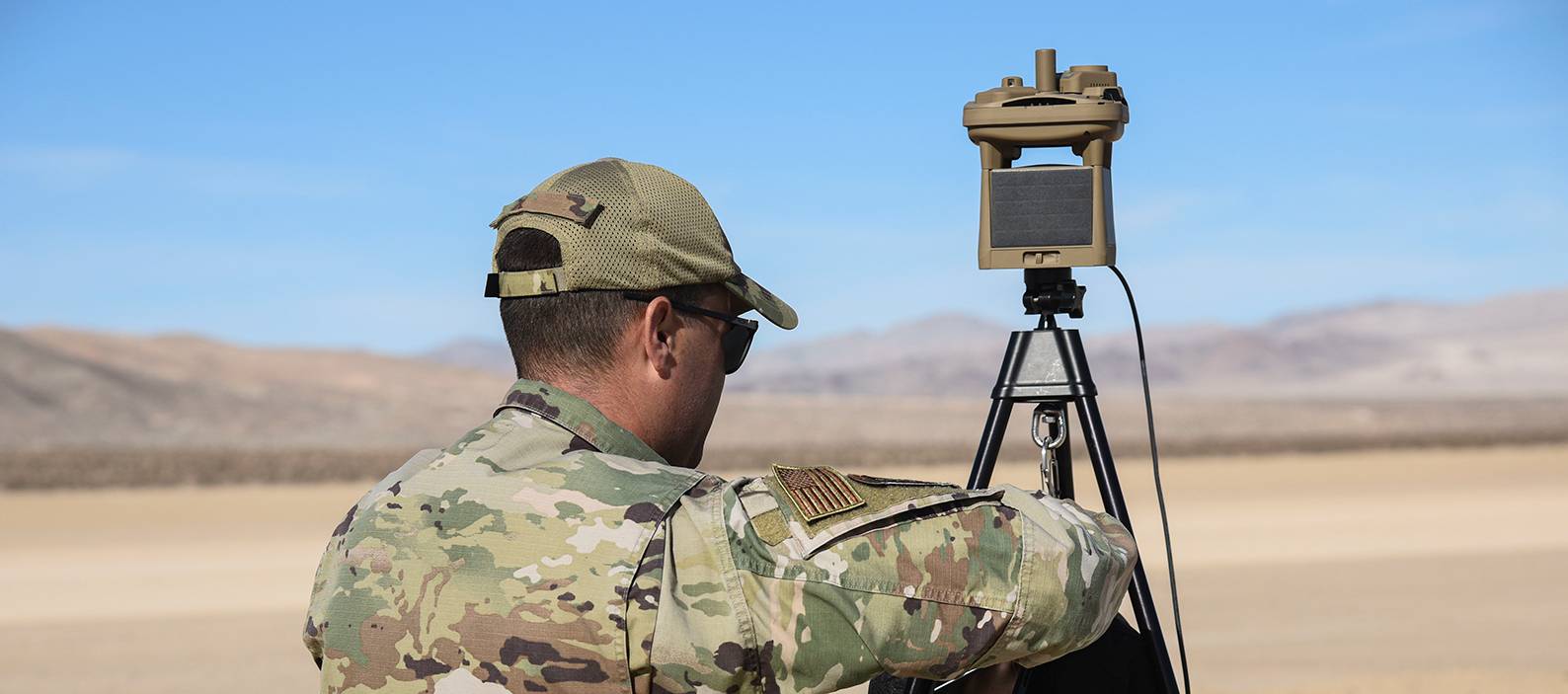 Army soldier sets up a remote weather station on a dry lake bed in the desert